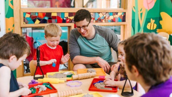 Kids and caregiver play with kinetic sand using various plastic tools