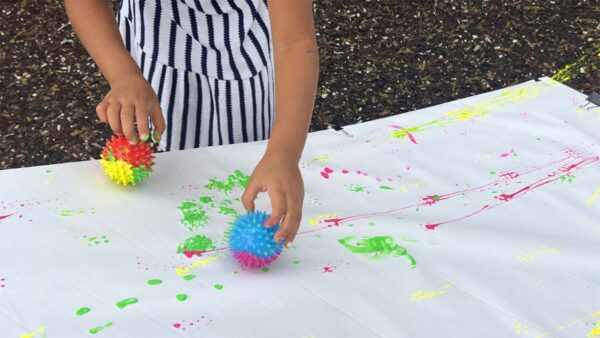 A child using rolling objects to paint on a ramp